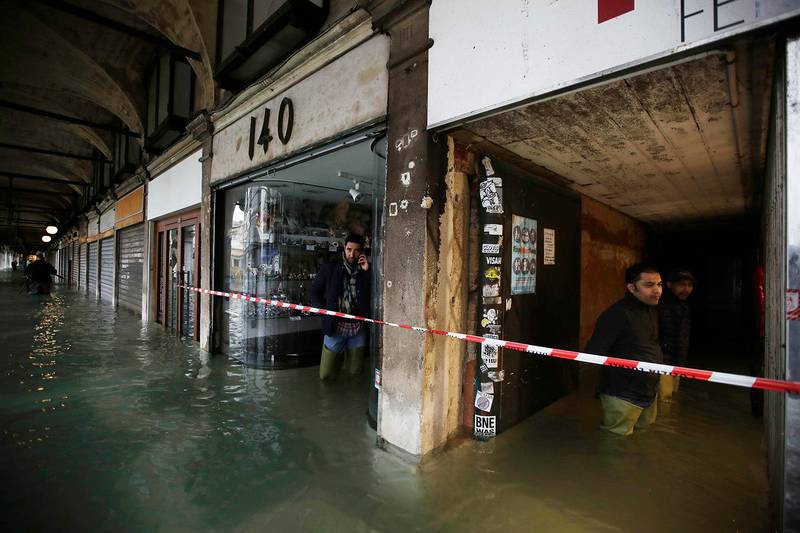 People stand near shops in a flooded St. Mark's Square in Venice, Italy, Friday, Nov. 15, 2019. The high-water mark hit 187 centimeters (74 inches) late Tuesday, Nov. 12, 2019, meaning more than 85% of the city was flooded. The highest level ever recorded was 194 centimeters (76 inches) during infamous flooding in 1966. (AP Photo/Luca Bruno)
