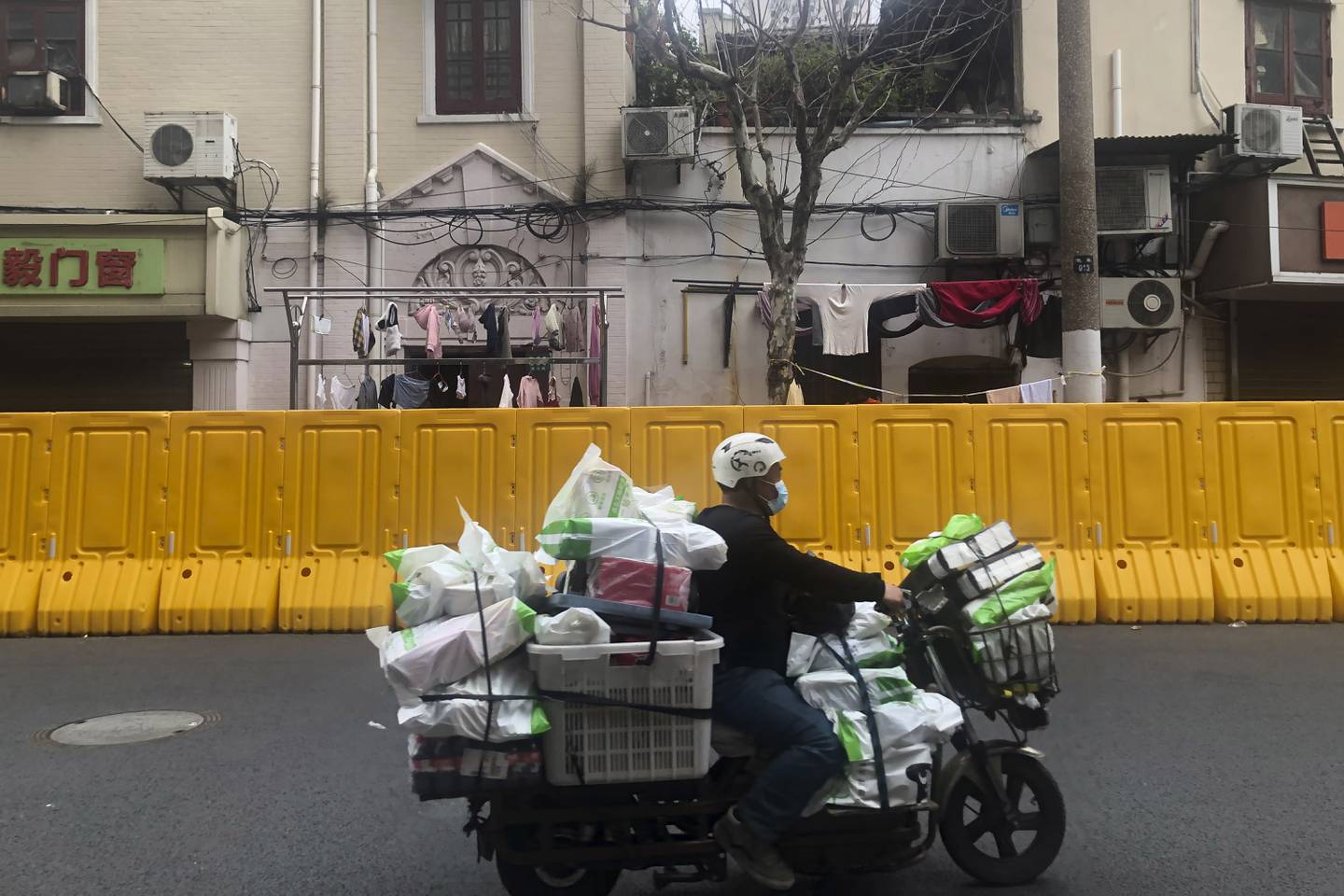 Et bud passerer en barriere som er satt opp for å holde folk hjemme i Shanghai. Innbyggere øst i byen, som håpte å komme ut av hjemmene sine etter fire dager torsdag, har fått dårlige nyheter. Noen må bli hjemme i minst ti dager til. Foto: Chen Si / AP / NTB