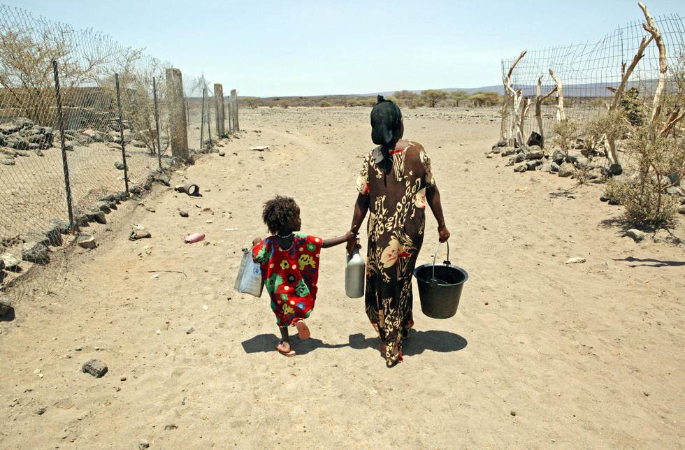 Bildet viser en kvinne som går på en tørre landevei i Djibouti. Hun holder et barn i hånden og har en bøtte i den andre.