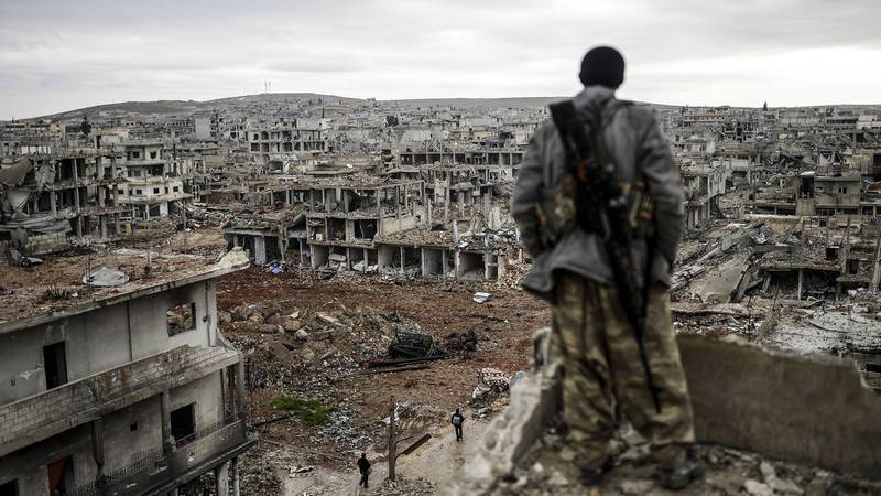 Bildet viser en mann som ser ut over en bombet by i Syria.