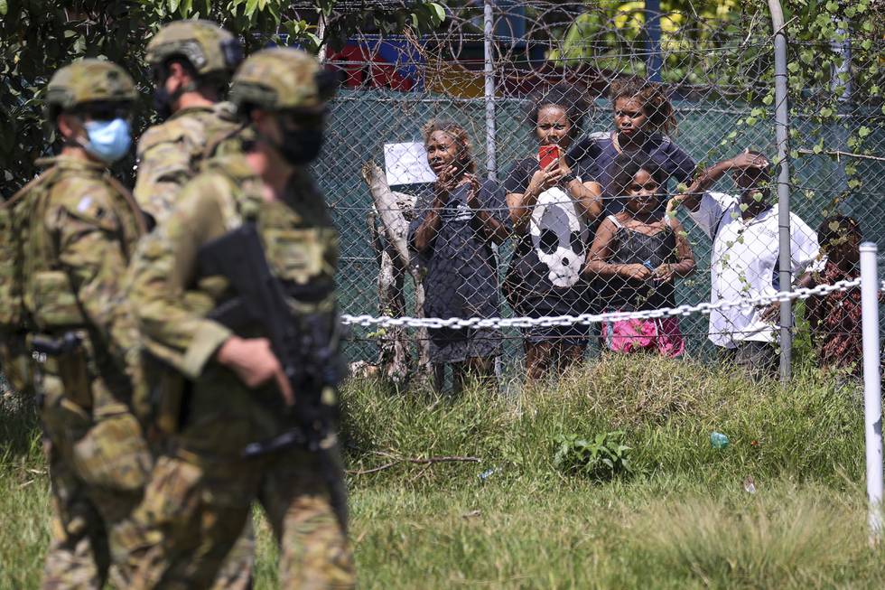 Bildet er av soldater fra Australia. De står foran et nettinggjerde med piggtråd på toppen. Bak gjerdet står en gruppe barn som tar bilde av soldatene. Foto: Gary Ramage via AP / NTB