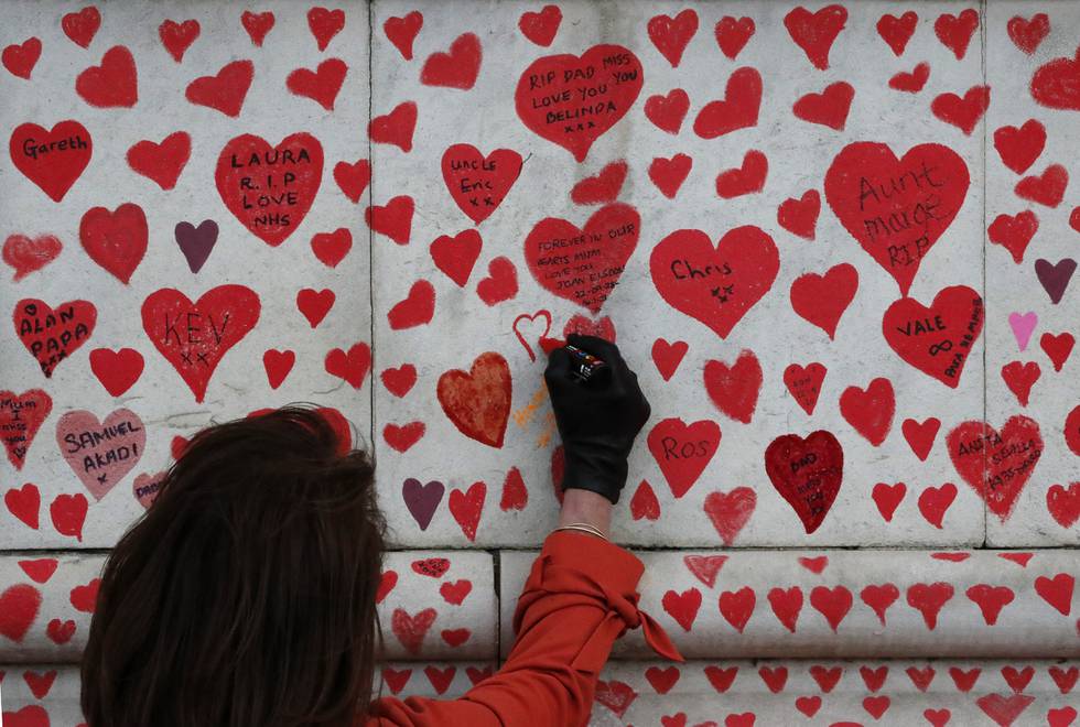 Bildet er av en kvinne som tegner et rødt hjerte på en murvegg. Hjertet som Fran Hall tegner er et av over 150.000 hjerter som er tegnet på denne muren. De er for å minnes nære og kjære som er døde med korona. Foto: Frank Augstein / AP / NTB