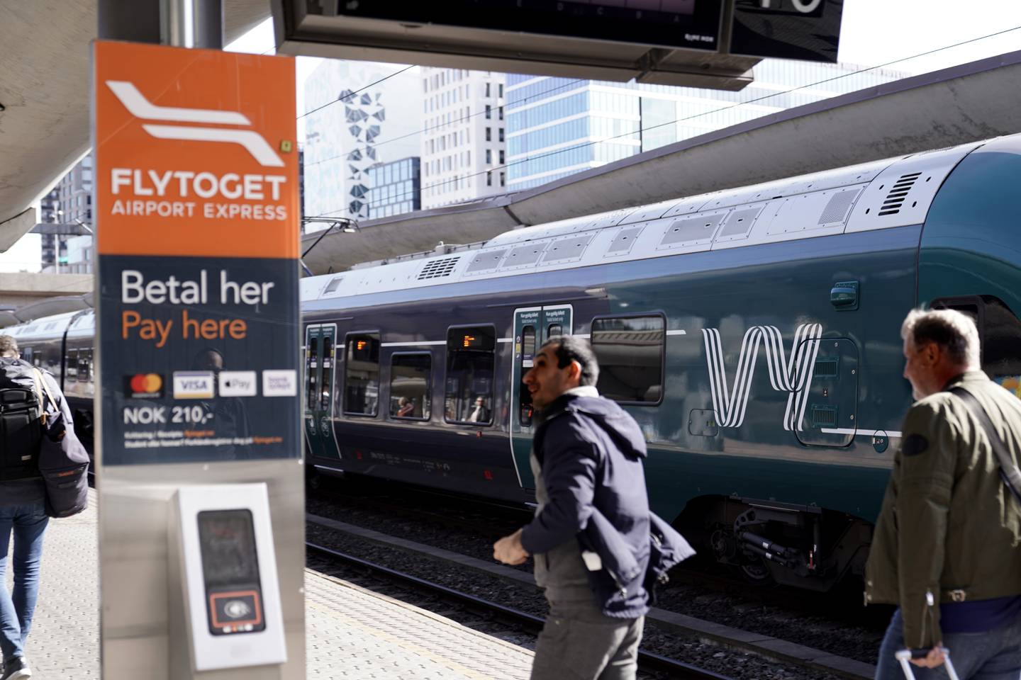 Bildet er av folk som går langs en jernbaneplattform. Til venstre er et skilt med billettsalg for Flytoget. Til høyre står et grønt og sølvfarget tog fra Vy. Foto: Håkon Mosvold Larsen / NTB