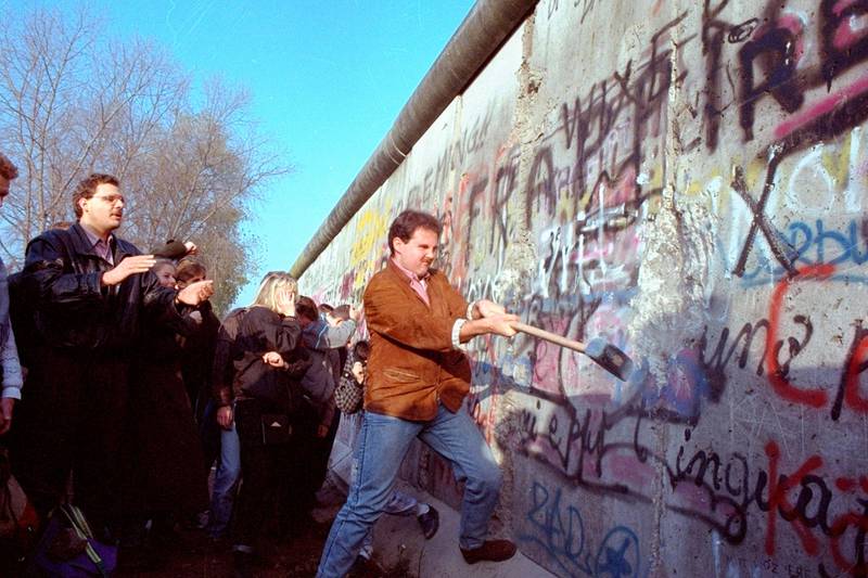 Bildet viser en mann som slår med en slegge mot Berlinmuren.
