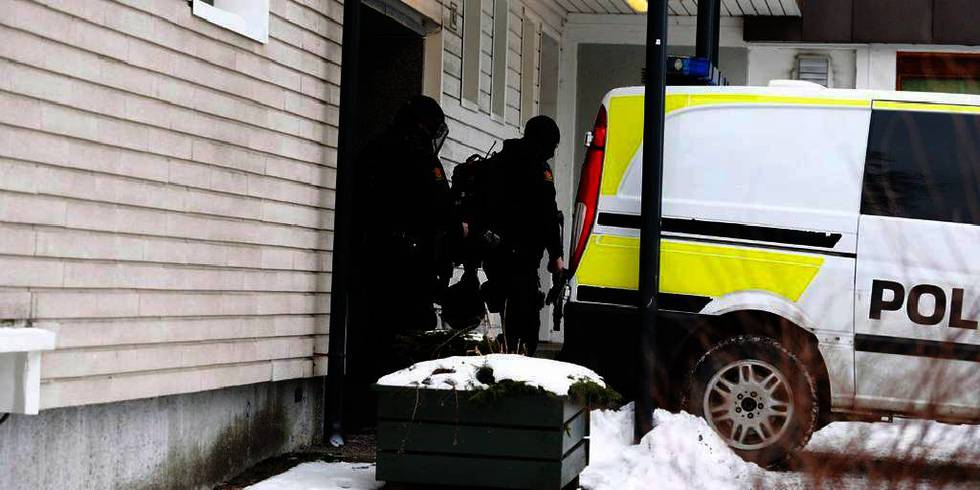 Bildet viser en politimann på vei ut av en leiliget i Oslo. Politimannen bærer et våpen.