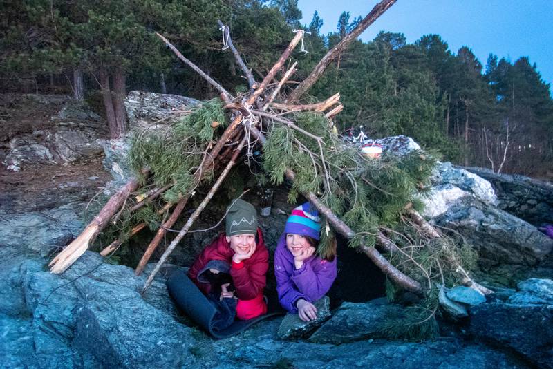Bildet er av to barn som har lagt seg i en gapahuk. De har på varmt tøy og lue.