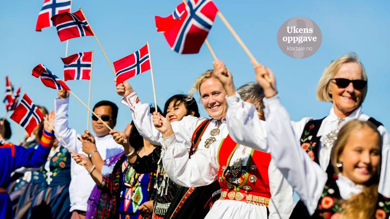 Bildet viser glade folk som feirer 17. mai i bunader og med flagg.