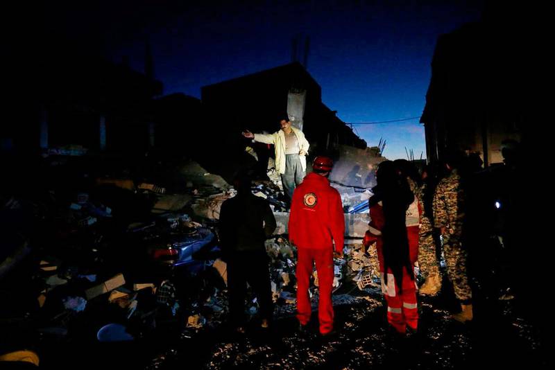 Bildet viser redningsfolk i Iran som står på en haug av ruiner. Det er mørkt.
