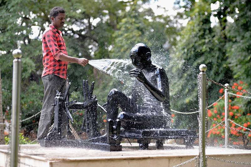 Bildet viser en mann som spyler en statue av Gandhi.