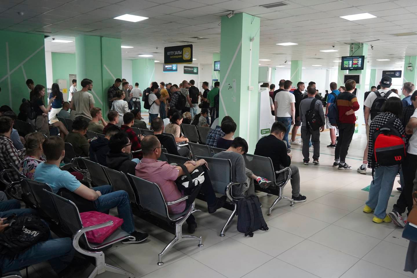 Folk står og sitter inne på et venteværeslet. De vil komme inn til Kasakhstan.