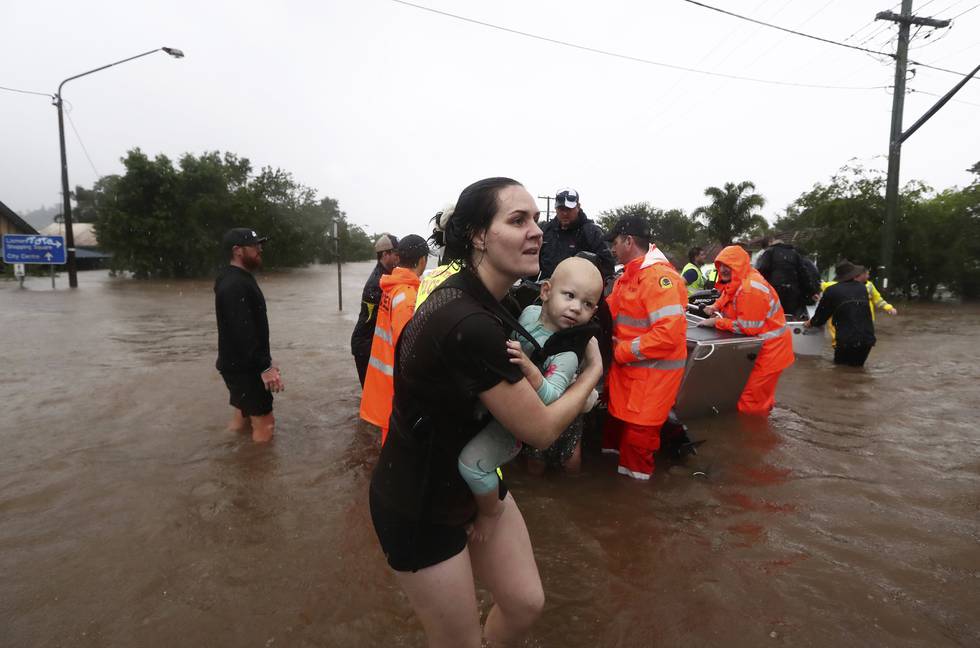 Bildet er av en kvinne som bærer en baby. I bakgrunnen er det redningsarbeidere. Der er de omgitt av redningsmannskaper.
Foto: Jason O'Brien / AAP / AP / NTB