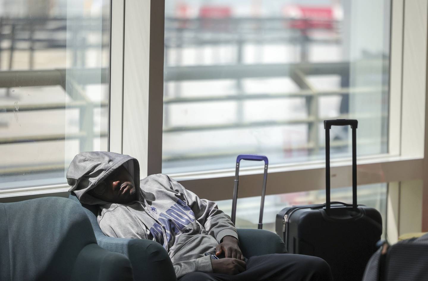 Bildet er av en mann i hettegenser. Han sitter i en stol ved et vindu og sover omgitt av bagasje. Foto: Oliver Matthys / AP / NTB