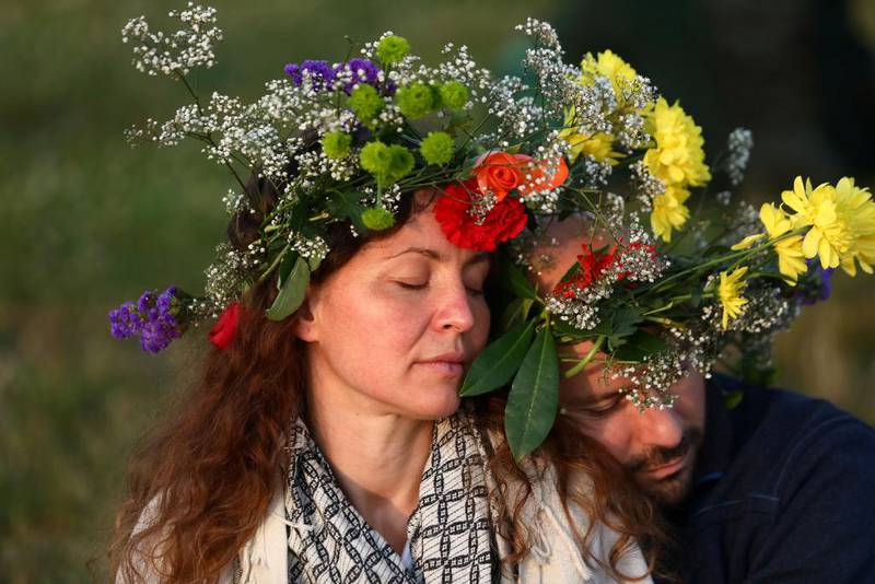 Bildet viser en kvinne og en mann med hver sin store blomsterkrans på hodet. Begge lukker øynene. Han har lagt hodet på skulderen hennes. De ser fredelige ut.