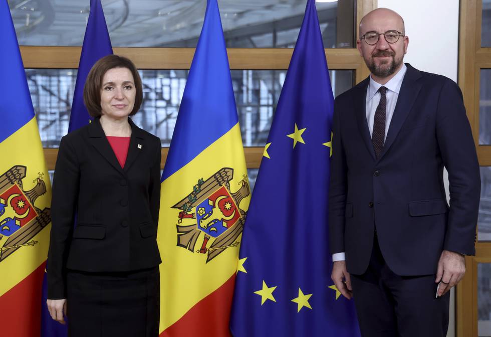 Bildet er av Maia Sandu og Charles Michel. De står foran flaggene til Moldova og EU. Sandu er president i Moldova og Michel i EU. EU-flagget er blått, med en sirkel gule stjerner. Moldovas flagg er delt i tre fra topp til bunn. Til venstre er det blått. I midten er det gult. Og til høyre er det rødt. I midten er også en ørn og et våpenskjold. Arkivfoto: Kenzo Triboillard / AP / NTB