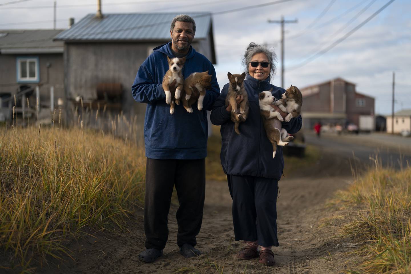 Sadie McGill og ektemannen Tracy McGill med valper avlet for å være sledehunder. De vil gjerne fortsette å leve livet her i inuittlandsbyen Shishmaref i Alaska, men frykter at klimaendringene en dag vil gjøre det umulig. Foto: Jae C. Hong / AP / NTB
