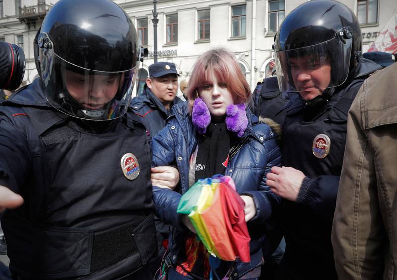 Bildet viser en person med regnbue-paraply som blir ført bort av politiet.
