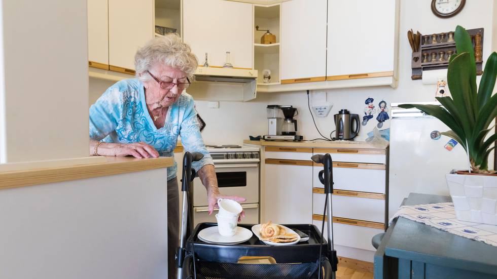 Bildet viser en eldre dame som setter kaffekopper og tebrød på rullatoren sin.