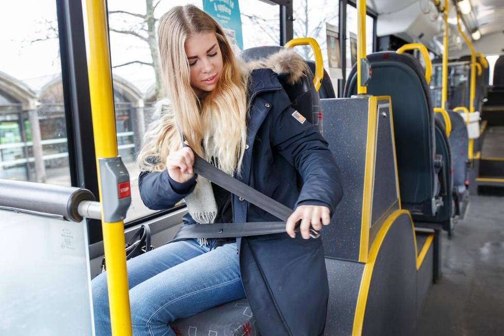 Bildet viser en jente på bussen som tar på seg belte.