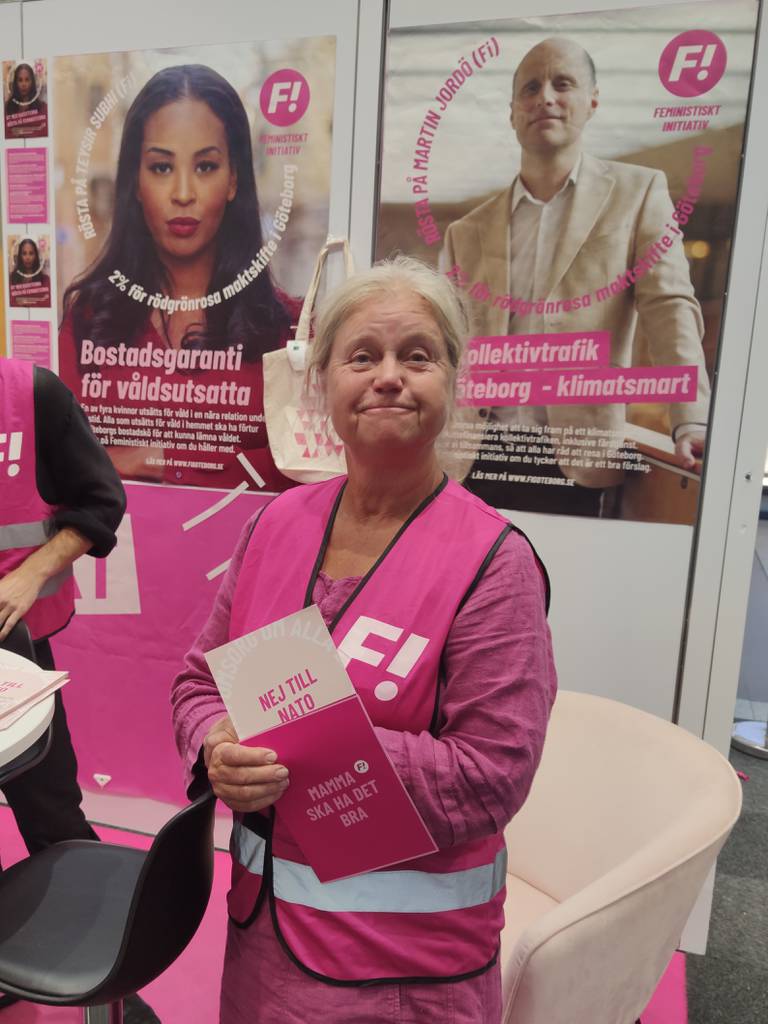 Bildet er av Cajsa Ottesjö som står på valgstand for Feministisk Initiativ (F!) Hun har rosa refleksvest med logoen, som passer med kjolen hun har under. Hun holder opp en valgseddel med slagordet "Nei til Nato" og en som sier at "Mamma skal ha det bra". Foto: Arnfinn Storsveen / Klar Tale