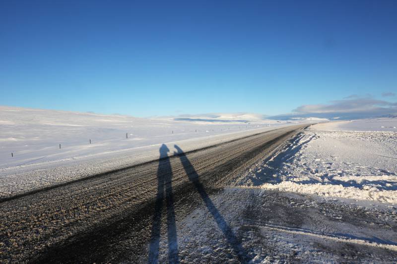 Bildet viser øde vei og snø, og skyggene av to mennesker.