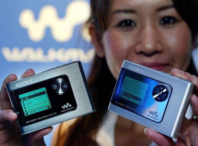 Bildet viser en dame som holder fram to Walkmans. Disse er digitale og nyere versjoner enn den orginale.