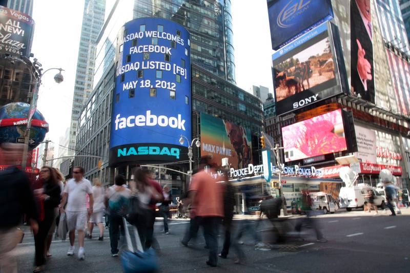 Passers-by in New York's Times Square walk near Nasdaq's giant monitor as Facebook's stock is set to begin trading on the Nasdaq stock market, Friday, May 18, 2012. (AP Photo/Bebeto Matthews)