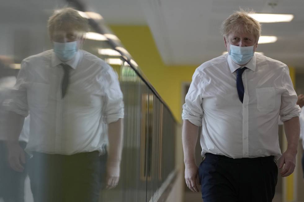 Bildet er av Boris Johnson på besøk på et sykehus. Han har dressbukse og hvit skjort. Han har på munnbind. Han står i en korridor. Foto: Frank Augstein / AP / NTB