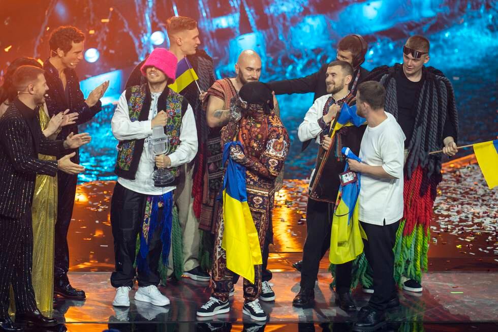 Bildet er bandet Kalush Orchestra som står på scenen og tar imot trofeet etter at de vant finalen i Eurovision Song Contest i Pala Olimpico i Torino i mai. De har med seg ukrainske flagg. Foto: Heiko Junge / NTB