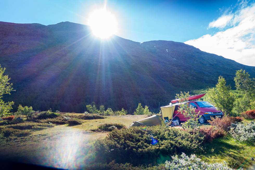 Bildet viser et telt og en bil som står ute i naturen. I bakgrunnen er sola på vei opp bak en fjellrygg. Det er småbusker og lyng i mye av bildet.
