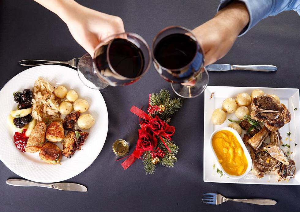 Bildet viser en tallerken med ribbe og en med pinnekjøtt. To hender skåler i rødvin. De fleste spiser den samme maten på julaften hvert år. 