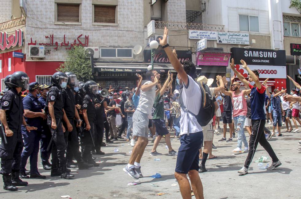 Bildet er av folk som protesterer i gatene i Tunis. Det er hovedstaden i Tunisia. De står ansikt til ansikt med politifolk med hjelmer og køller. Foto: Hassene Dridi / AP / NTB