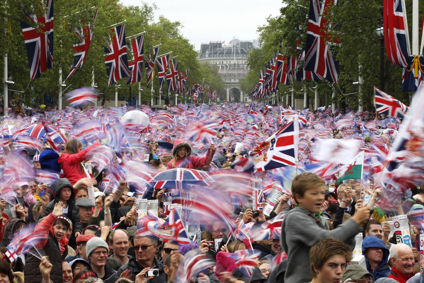 Bildet er av en folkemengde som står tett i tett. Det er britiske flagg overalt. Folk feirer  dronning Elizabeth. Foto: Sang Tan / AP / NTB