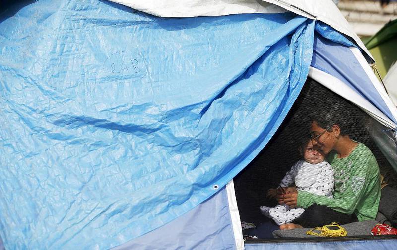 Bildet viser et eldre barn som holder en baby. De sitter i en teltåpning.