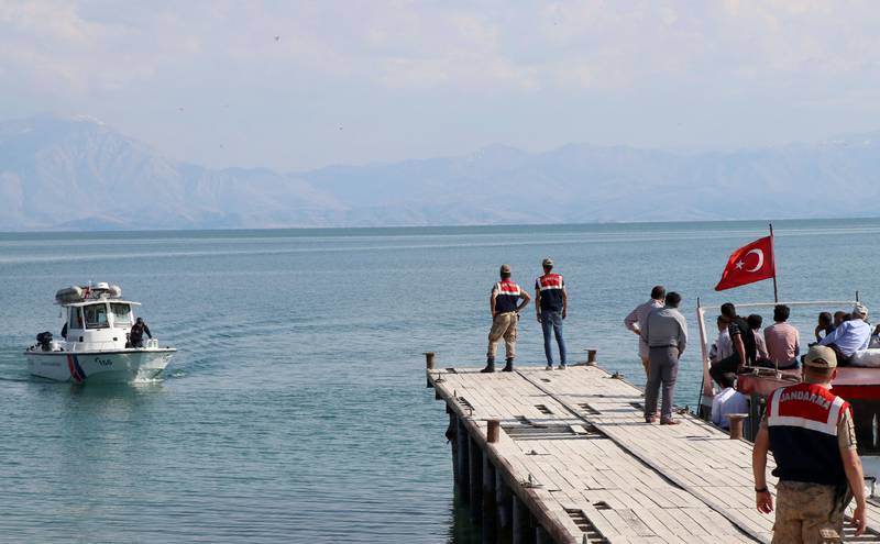 Bildet er tatt fra en brygge ved Vansjøen. En båt med tyrkisk flagg har vært ute for å lete etter druknede. På brygga står det flere mennesker.