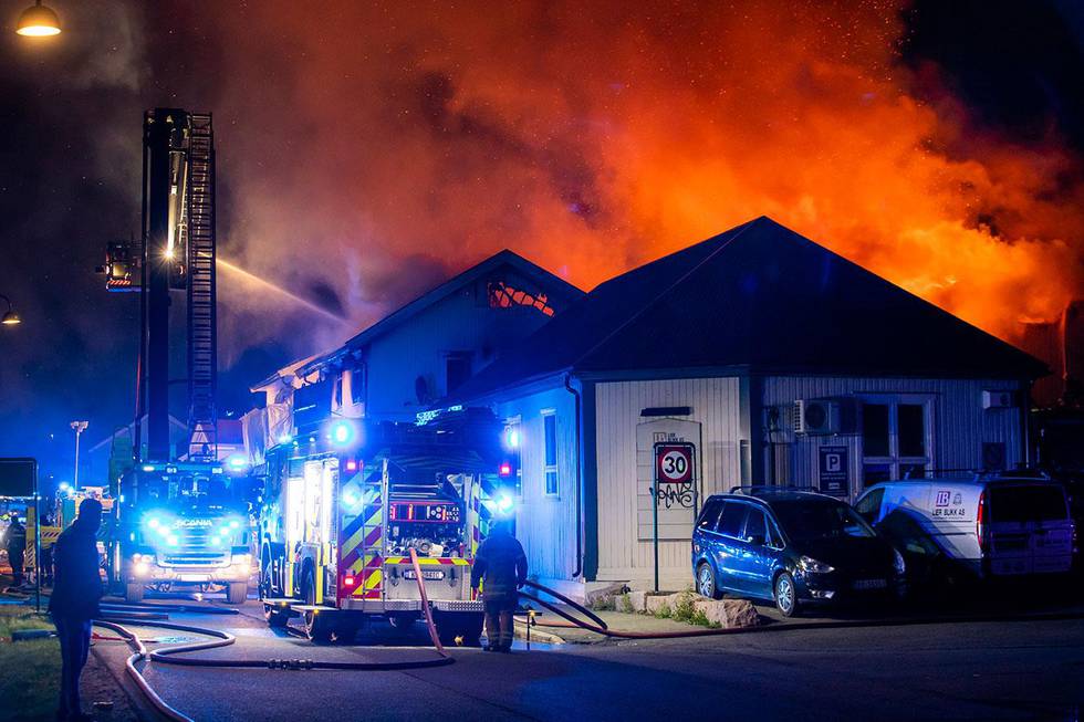 Bildet viser flammer og røyk som stiger opp fra noen trehus. En brannbil er på steder og brannmannskaper jobber med å slokke. Natt til søndag brant det i tre hus i Lier i Buskerud. To personer døde og to ble skadd. 