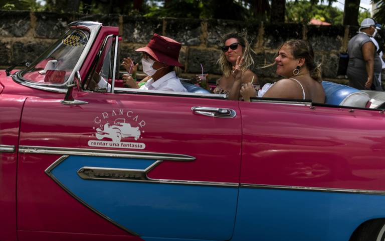 Bildet er av en rød og blå bil uten tak. To amerikanske turister sitter i baksetet. Foto: Ramon Espinosa / AP / NTB