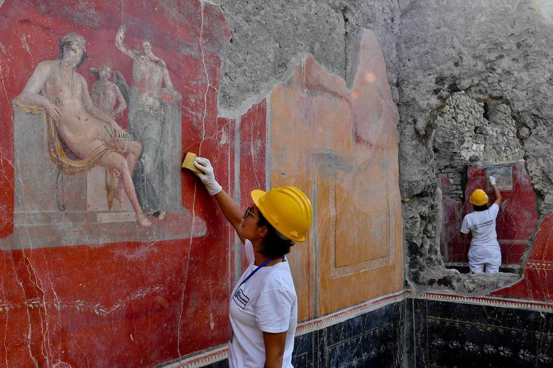 Bildet viser en arkeolog som graver frem en rød vegg i Pompeii