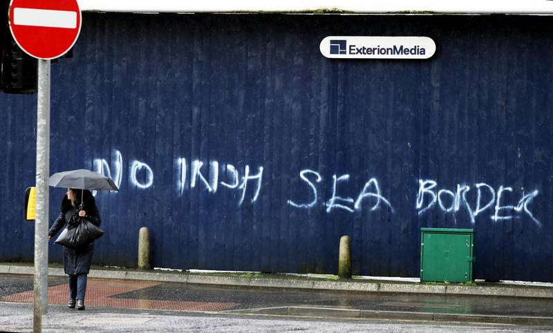 Bildet er av en kvinne som står under en paraply i regnet. I bakgrunnen er en flere meter lang grafitti på en vegg. Budskapet er motstand mot en grense i sjøen mellom Nord-Irland og resten av Storbritannia.