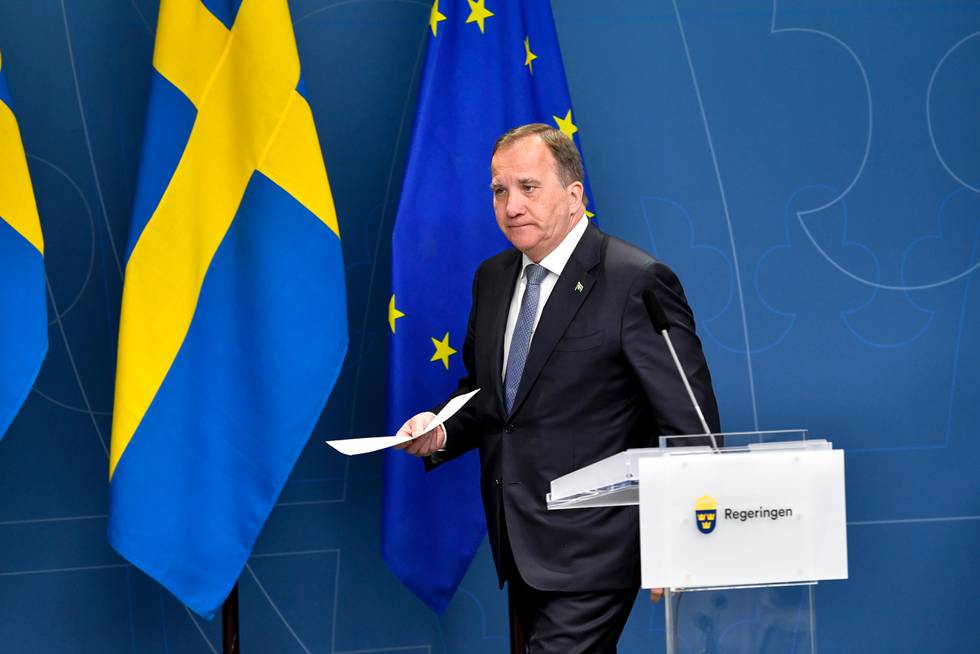 Bildet er av Sveriges statsminister Stefan Löfven. Han holder en bunke ark og går mot en talerstol. Veggen bak er lyseblå. Det henger både svenske flagg og EU-flagg foran veggen.