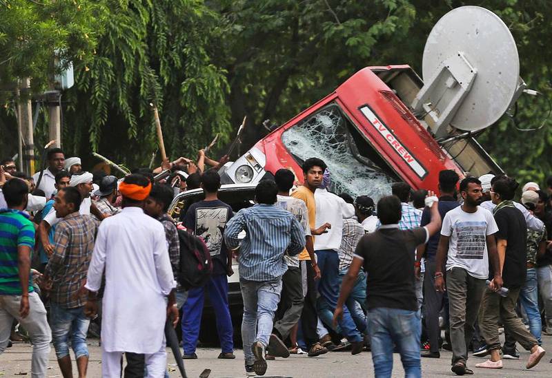 Bildet viser en nyhetsbil som blir veltet og ødelagt av mange menn i India.