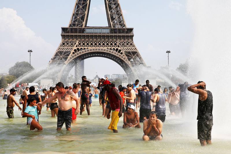 Bildet viser folk som kjøler seg ned i en fontene foran Eiffeltårnet i Paris i Frankrike.