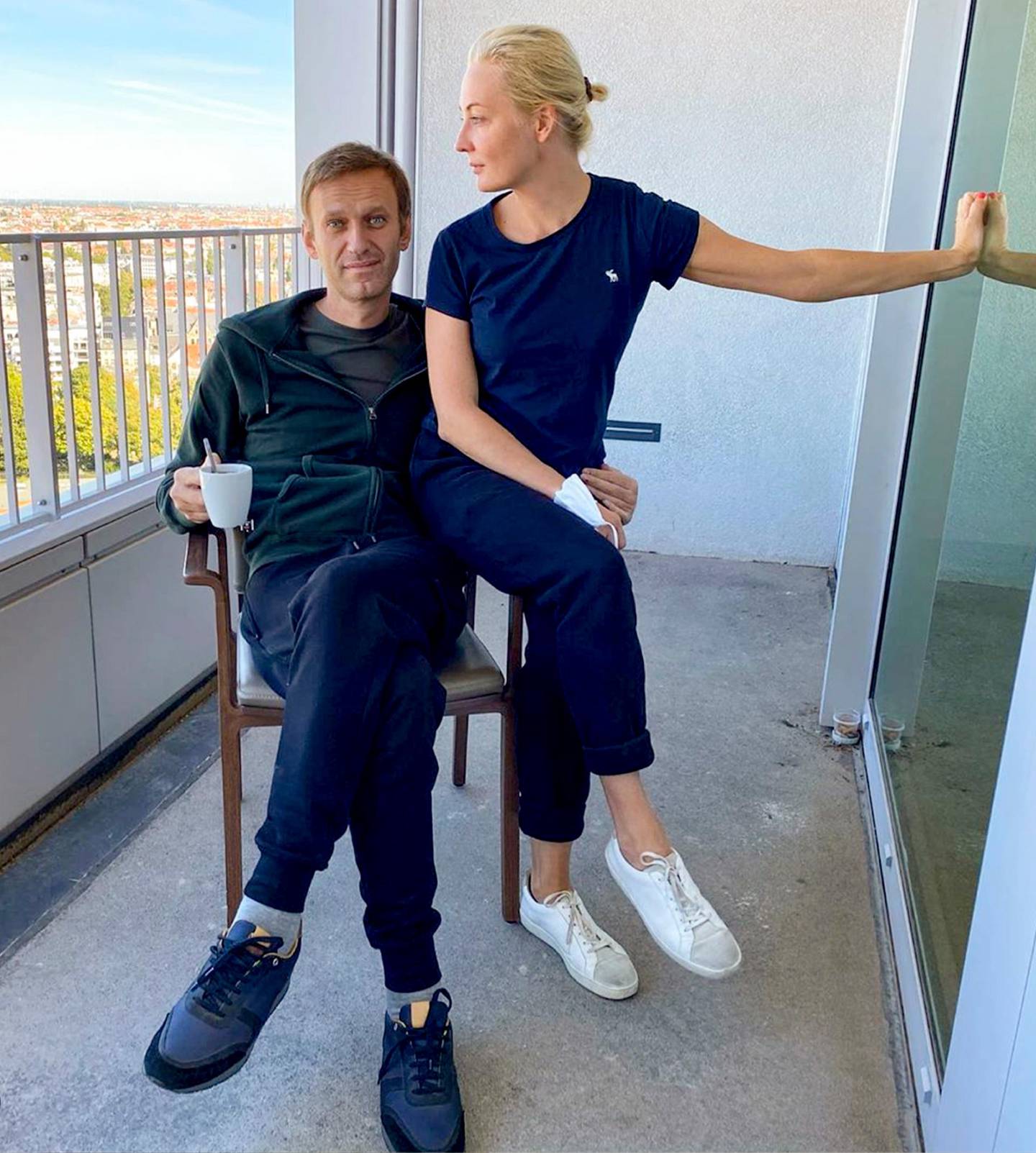 Bildet er av Aleksej Navalnyj sammen med sin kone Julia på sykehuset i Berlin. Han sitter på en stol på en balkong. Hun sitter på armlenet og støtter eg med en hånd mot veggen.