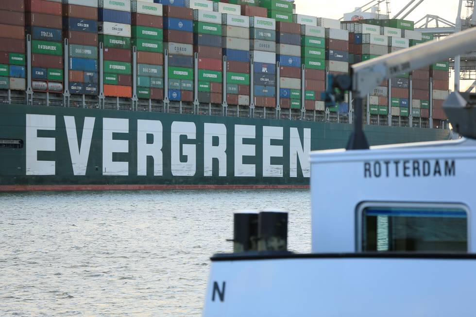 Bildet er av den ene siden av skipet Ever Given. Det står Evergreen i hvitt på siden av det mørkegrønne skipet som er lastet med store mengder konteinere i ulike farger. I forgrunnen av bildet er også en liten hvit båt der det står Rotterdam. Foto: Eva Plevier / Reuters / NTB