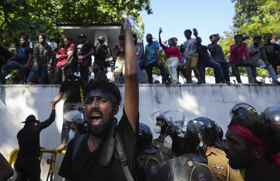 Bildet er av folk som protesterer i Sri Lanka. Det står folk oppe på en mur i bakgrunnen. I front står en mann og roper inn i en megafon mens han holder en hånd i været. Foto: Eranga Jayawardena / AP / NTB