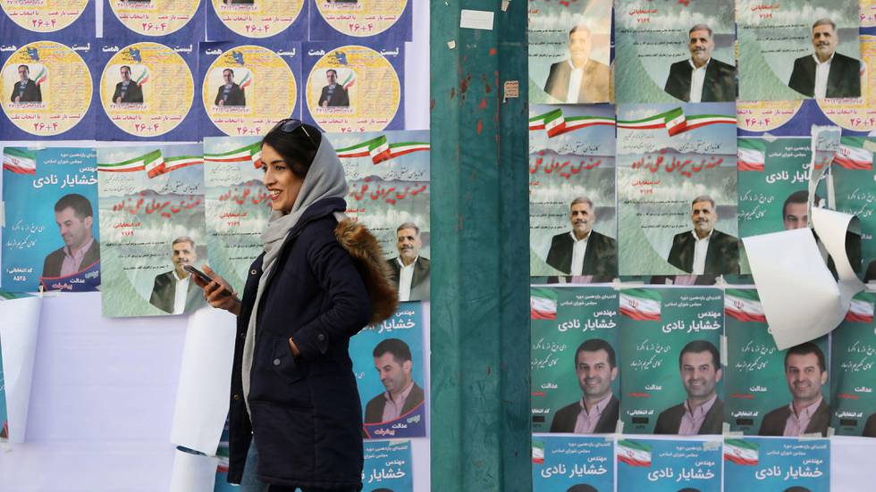 Bildet viser en iransk kvinne som går forbi bilder av kandidater i Teheran. Fredag er det valg på ny nasjonalforsamling.