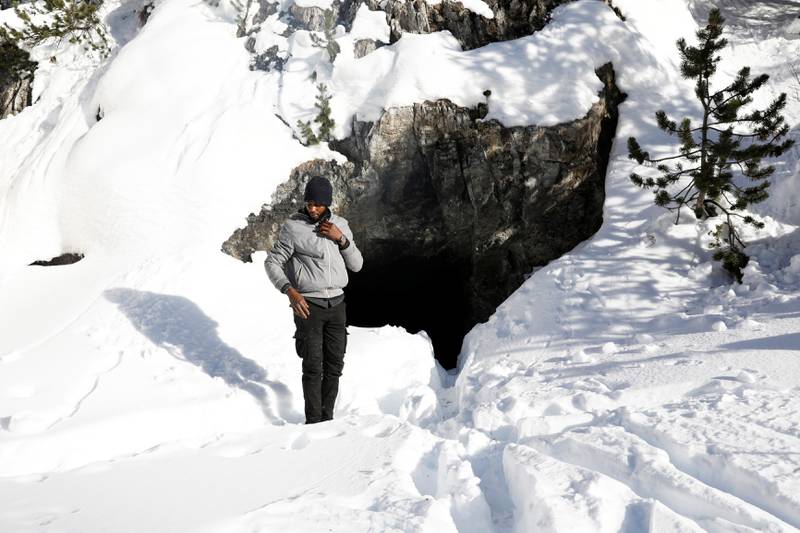 Bildet viser en mann som står foran en hule i fjellet.
