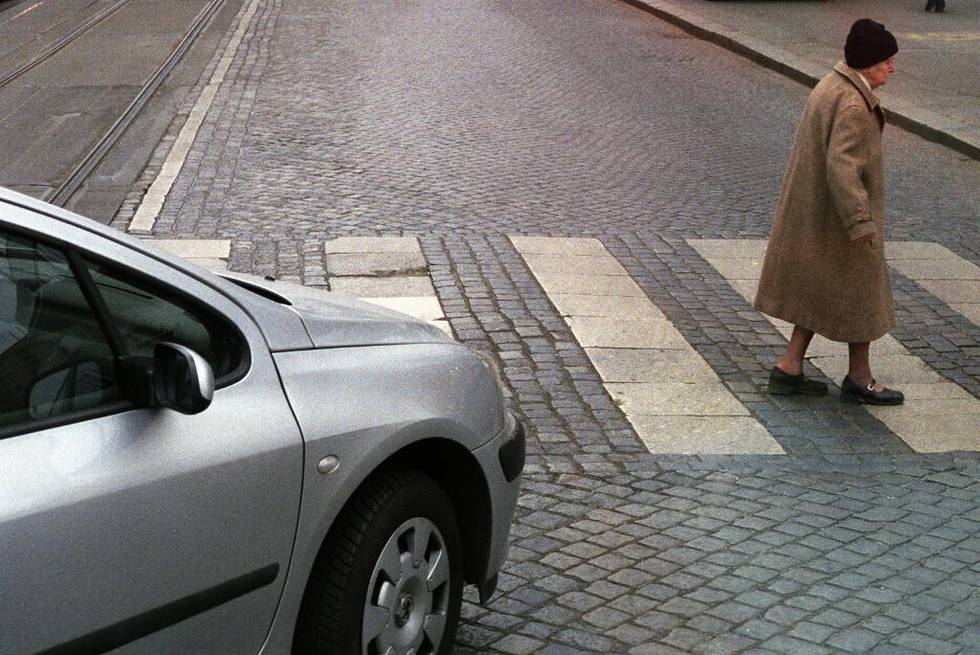 Bildet viser en eldre dame som går over et gangfelt. En bil venter på å kjøre over. 