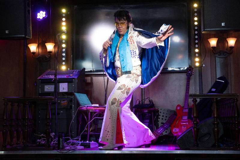 Bildet viser Kjell Elvis på en scene i Oslo. Han har hvis dress, lys blå skjorte, kappe og solbriller.