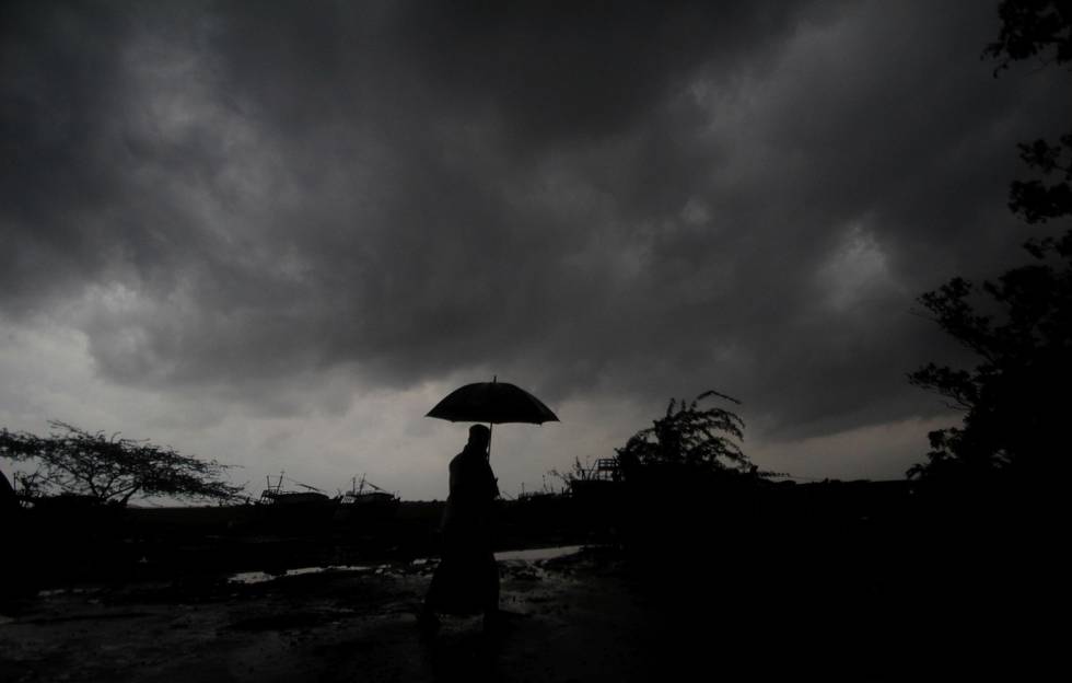 En person som står med paraply og ser opp mot de mørke skyene.