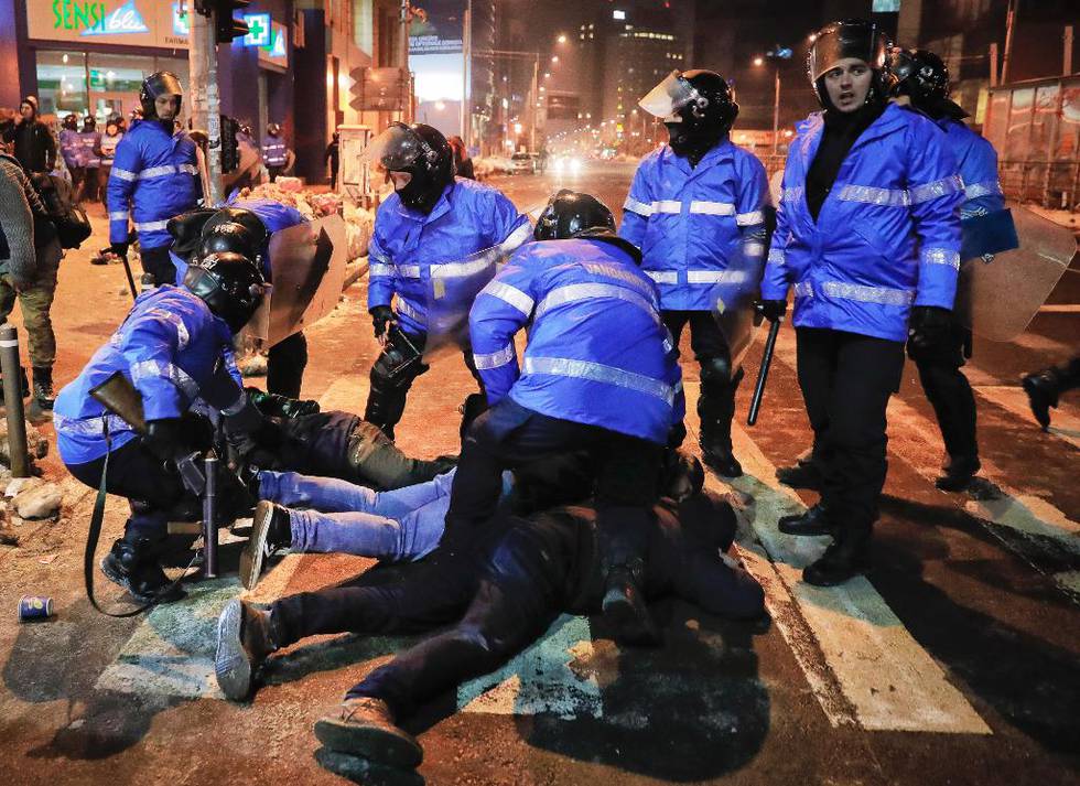Bildet viser politiet som holder demonstranter nede på bakken. Folk protesterer mot ny lov i Romania.